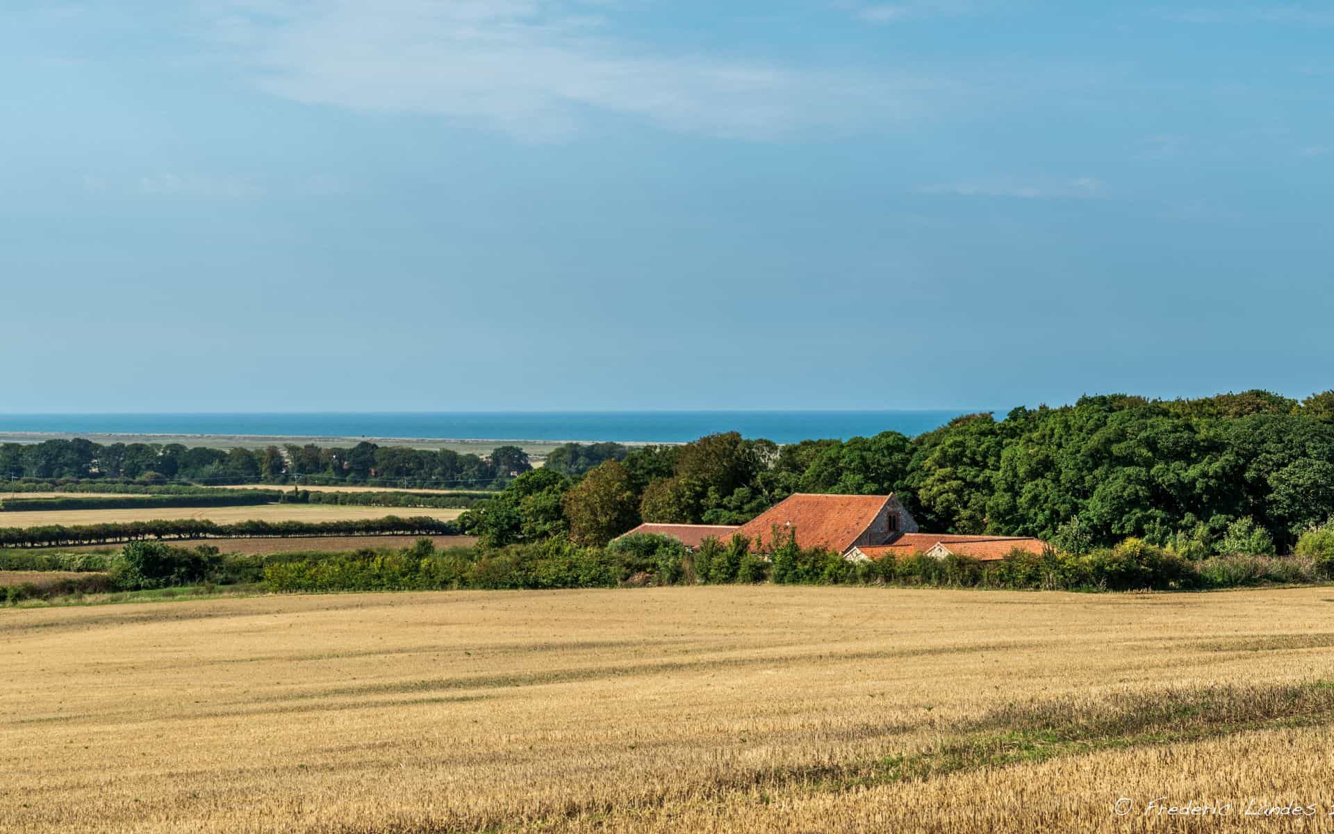 A lush Norfolk countryside with fields, trees, and a distant view of the sea, perfect for camping an.