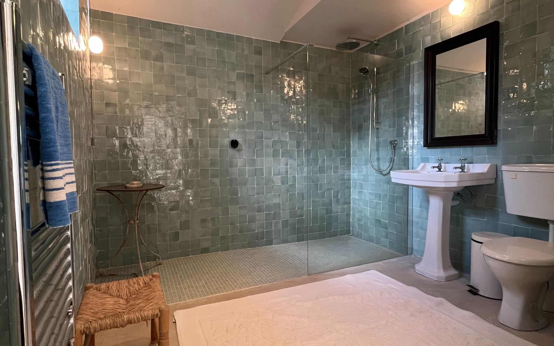 A lush, modern bathroom with green tiled walls, walk-in shower, and classic white fixtures at The St.