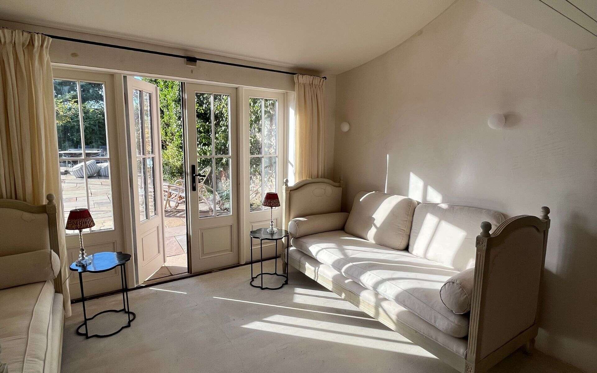 A lush, bright living room with large glass doors opening to a garden, featuring elegant cream sofas.