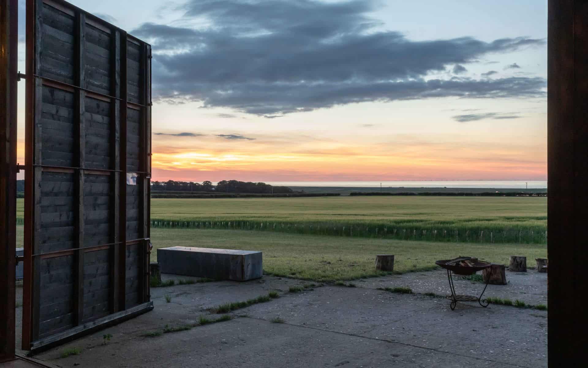 Rustic barn opening with scenic Norfolk sunset view over flat farmland and open skies.