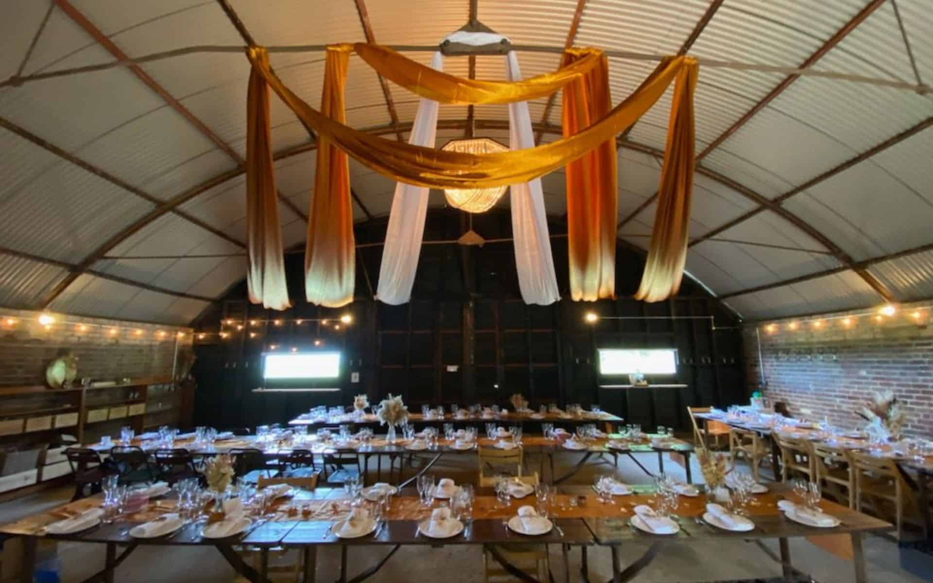 Elegant barn wedding reception setup at The Hanger, Barn Drift Norfolk with draped fabric and warm l.