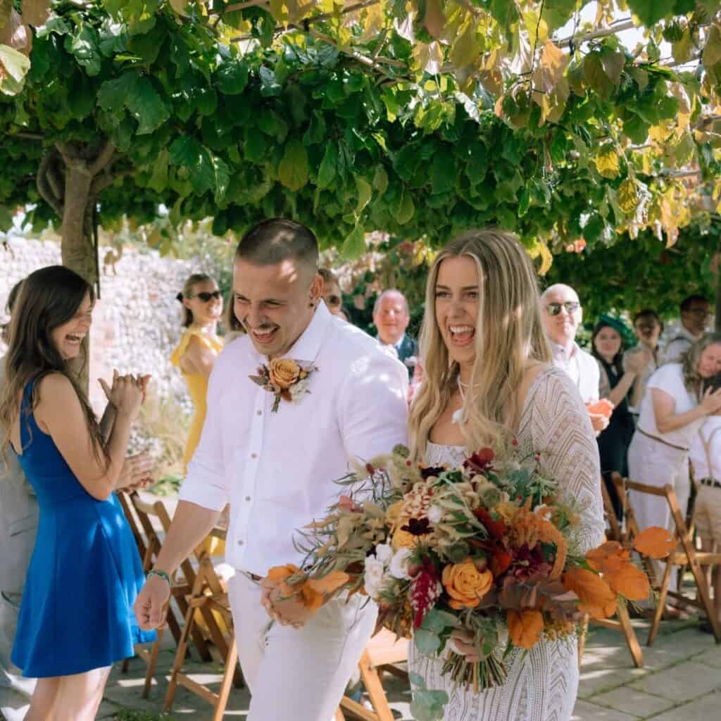 Joyful wedding couple under garden trees at Norfolk wedding venue. Barn Drift